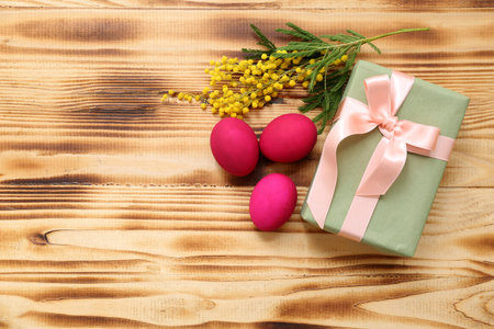 Painted Easter eggs, gift box and mimosa flowers on wooden background