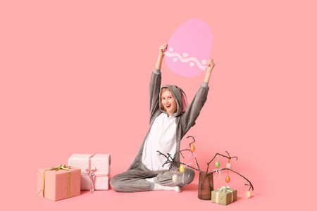 Beautiful young happy woman in bunny costume with gift boxes and decorations on pink background....