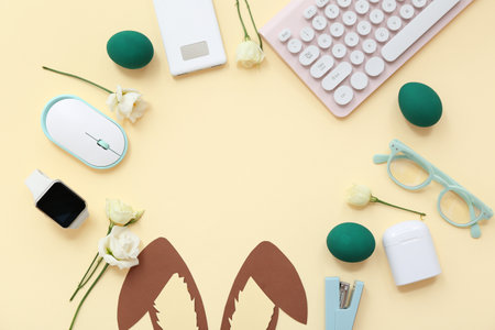 Frame made of Easter eggs, paper, bunny ears, glasses, flowers, computer keyboard and mouse on yellow backgroundの写真素材