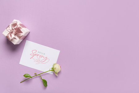 Greeting card with text HELLO SPRING, beautiful white rose and gift box on lilac backgroundの写真素材