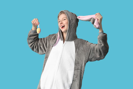 Beautiful young woman in bunny costume with decorative egg on blue background. Easter celebration