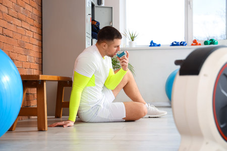 Sporty young man with asthma attack using inhaler in gym