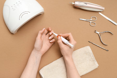 Female hands applying cuticle oil onto fingernails, manicure instruments and towel on brown backgroundの写真素材