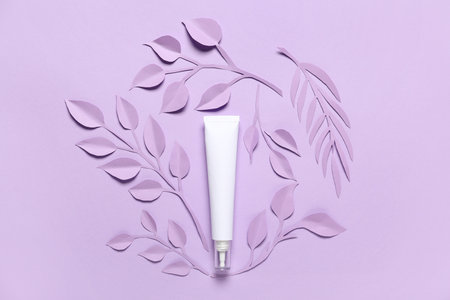 Tube of cosmetic product, paper flowers and leaves on color backgroundの写真素材