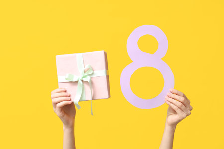 Female hands with paper figure 8 and gift box for International Women's Day on yellow background, closeupの写真素材
