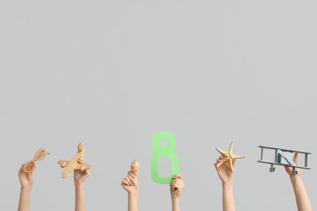Female hands with paper figure 8, toy planes and sunglasses on gray background. International...