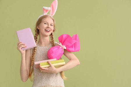 Young girl with Easter bunny ears, books and gift on color background
