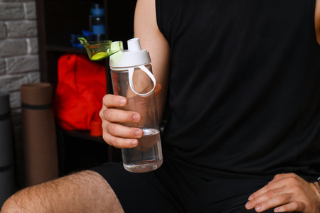 Sporty young man with water bottle in locker room, closeupの写真素材