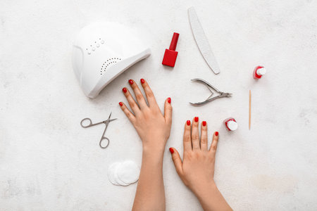 Female hands with stylish red nails and manicure equipment on white grunge backgroundの写真素材