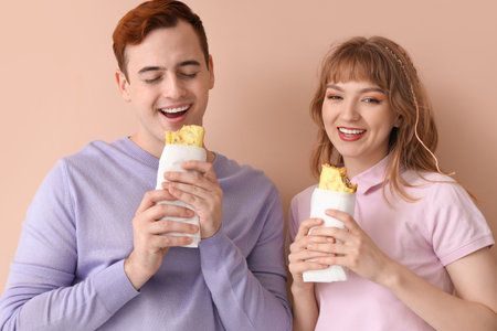 Young couple with tasty sandwich wraps on beige backgroundの写真素材