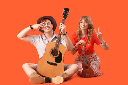 Couple of hippies with guitars showing victory gesture on orange backgroundの写真素材