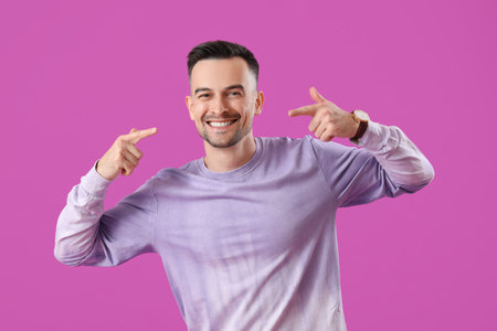 Young man pointing at his smile on purple backgroundの写真素材