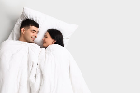 Young couple with pillow and blanket on light backgroundの写真素材