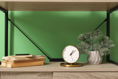 Shelving unit with houseplant, books and alarm clock near green wall