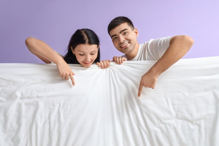 Young couple with blanket pointing at something on lilac backgroundの写真素材