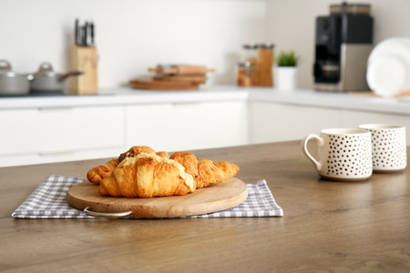 Wooden board with tasty croissants on table in modern kitchenの写真素材