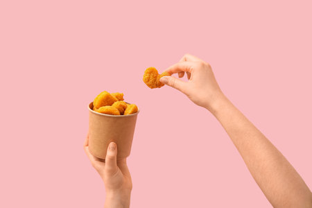 Woman holding paper bucket with tasty nuggets on pink backgroundの写真素材