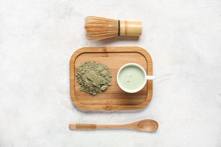 Wooden board with cup of fresh matcha tea, powder and accessories on light backgroundの写真素材