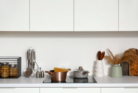 White counters with electric stove, cooking pots and utensils in modern kitchenの写真素材