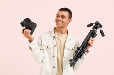 Male photographer with modern camera and tripod on pink background