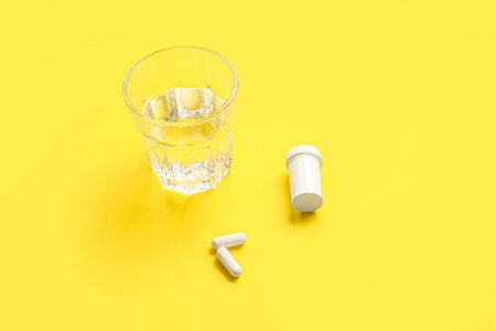 White pills and glass of water on yellow backgroundの写真素材