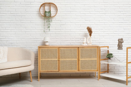 Modern light wooden chest of drawers with shelving unit and couch near white brick wall in roomの写真素材