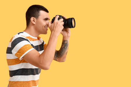 Male photographer with modern camera on yellow backgroundの写真素材
