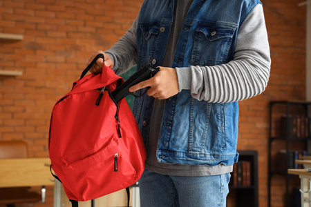 Male student with gun and backpack in classroom, closeupの写真素材