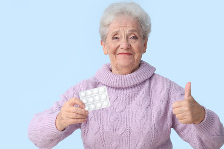 Senior woman with pills showing thumb-up on blue backgroundの写真素材