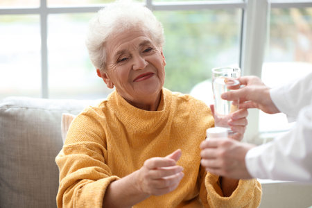 Senior woman taking pills and glass of water from doctor at homeの写真素材