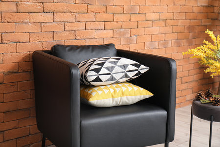 Black leather armchair with pillows near orange brick wallの写真素材