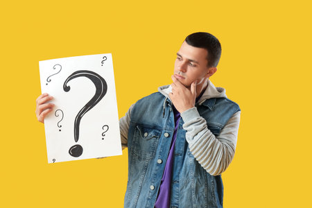Wondering young man holding paper with question marks on yellow backgroundの写真素材