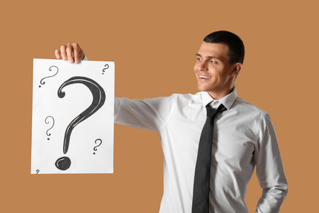 Young man holding paper with question marks on brown backgroundの写真素材