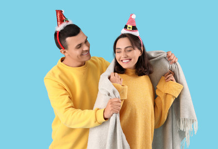 Happy young couple in Christmas hats with plaid on blue backgroundの写真素材