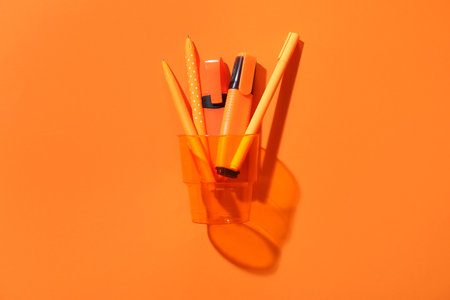 Pencils and pens in transparent glass on orange backgroundの写真素材