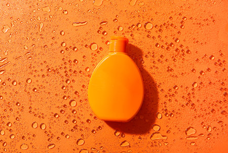 Bottle of sunscreen cream with water drops on orange backgroundの写真素材