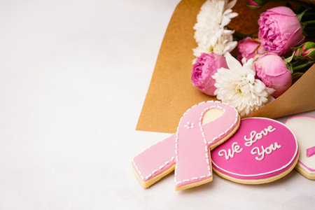Pink cookies with ribbon, text WE LOVE YOU and bouquet of flowers on white grunge background. Breast cancer awareness conceptの写真素材