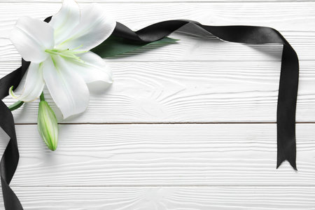 Frame made of beautiful lily flowers and black funeral ribbon on white wooden backgroundの写真素材