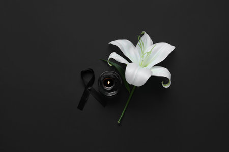 Beautiful lily flower with funeral ribbon and candle on black backgroundの写真素材