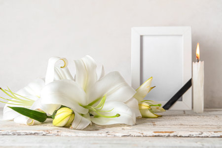 Beautiful lily flower and blank funeral frame on tableの写真素材