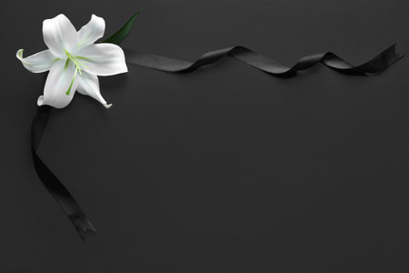Beautiful lily flower with funeral ribbon on black backgroundの写真素材