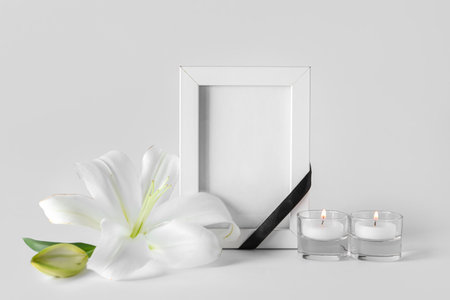 Blank funeral frame, burning candles and beautiful lily flowers on gray backgroundの写真素材