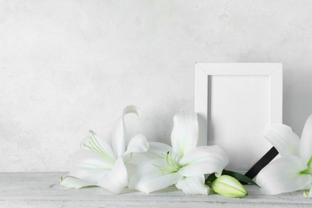 Blank funeral frame and beautiful lily flowers on tableの写真素材