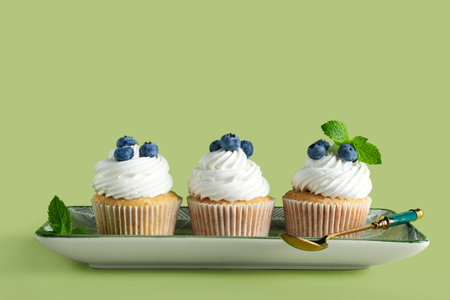 Plate of tasty cupcakes with blueberries on green backgroundの写真素材