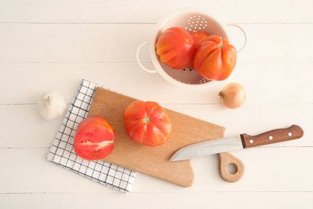 Board and colander with fresh ripe tomatoes on white wooden tableの写真素材