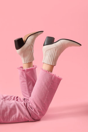 Legs of young woman in stylish beige leather boots on pink backgroundの写真素材