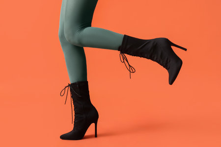 Legs of young woman in stylish black shoes on orange backgroundの写真素材