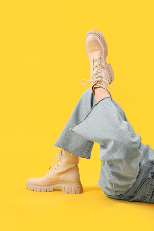 Legs of young woman in stylish beige leather boots on yellow backgroundの写真素材
