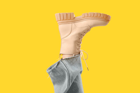 Leg of young woman in stylish beige leather boot on yellow backgroundの写真素材