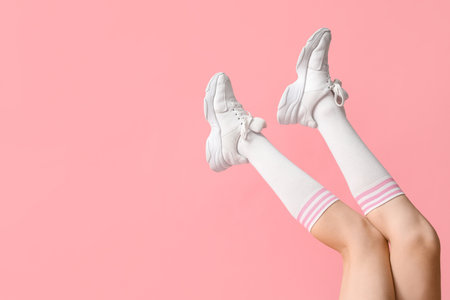 Legs of young woman in stylish white sneakers on pink backgroundの写真素材